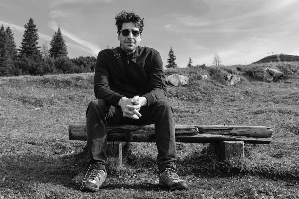 Sittig Fahr-Becker wearing sunglasses, seated on a wooden bench in an open landscape. Black-and-white photograph.