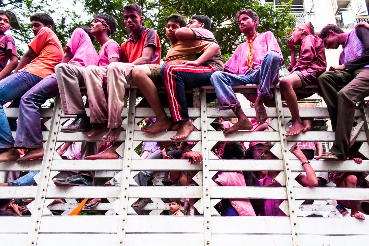 Festival participants covered in pink powder sit along the side of a white truck in Bombay.